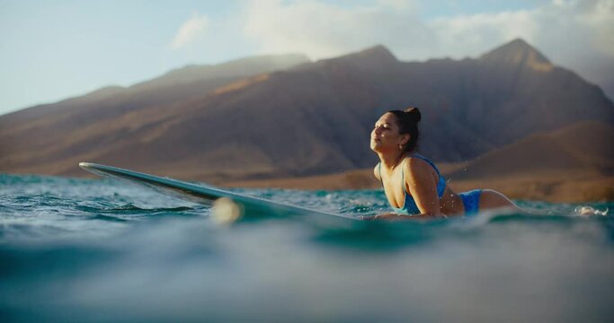 Beautiful Hawaiian surfer girl paddling out at sunset on her longboard