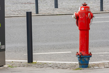 Red hydrant on a sidewalk next to a couple of black sidewalk poles