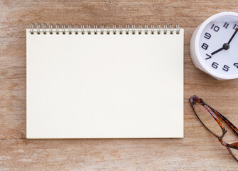 Top view, blank notebook and white clock show time 7 o' clock, eyeglasses on wooden table. Flat lay, space for your text..