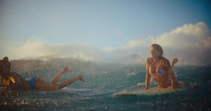 Surfer girls paddling out over the top of a wave at sunset in Hawaii, best friends surfing together, summer lifestyle