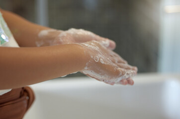Clean and protection from infection by a young girl washing her hands with foam soap in the bathroom for virus prevention. A child practicing hygiene and cleanliness by rinsing her palms in the sink