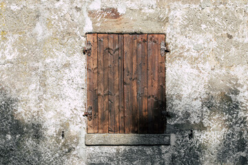 Fototapeta na wymiar old wooden window, stonewall cracked and rough, shadow on closed wooden shutter, no person