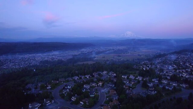 Drone footage flying over a residential neighborhood overlooking a valley with a view of Mt. Rainier during a late summer evening.