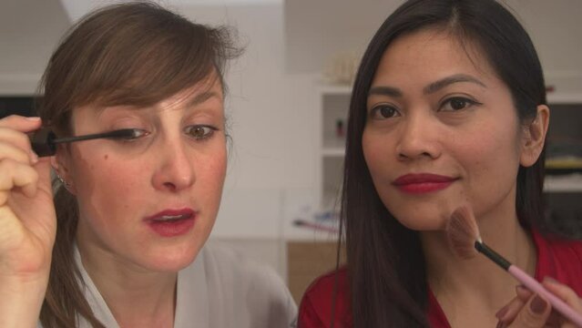 CLOSE UP: Two Ladies Using Make Up Products And Getting Ready For A Girls Night Out. Asian And Caucasian Woman Applying Facial Beauty Products. Cheerful Females Having Fun While Doing Their Make Up.