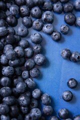 Vertical photo with scattered blueberries in a blue flat plate