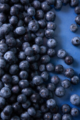 Vertical photo with scattered blueberries in a blue flat plate