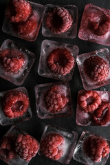 Fresh frozen in ice red raspberry on black background. Macro berries and ice cube for abstract background.