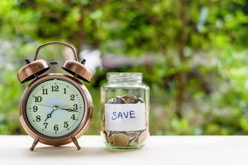 Fotobehang Saving money for sustainable life in the future concept : Coins in a clear glass jar with vintage clock nearby. Saving is money saved for education, paying taxes, insurance, health, travel and more .. © William W. Potter