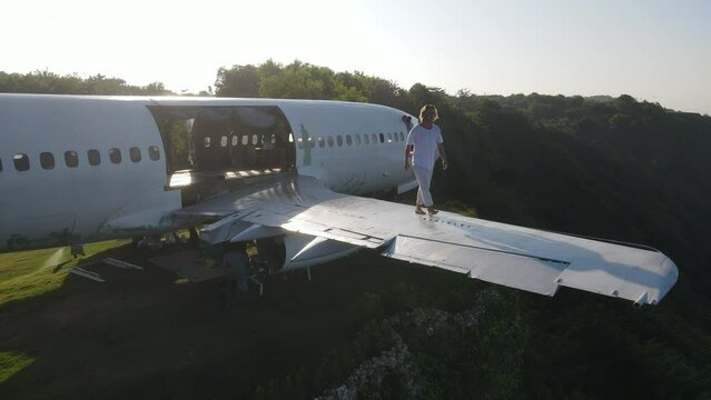 Handsome young man walks on the wing of an abandoned plane on a cliff in Bali