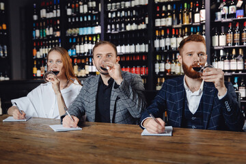 Friends tasting red wine sommeliers and taking notes at degustation notepad