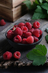 Fresh red raspberries in bowl on wooden dark baskground. Closeup berries background.