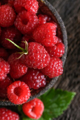 Fresh red raspberries in bowl on wooden dark baskground. Closeup berries background.