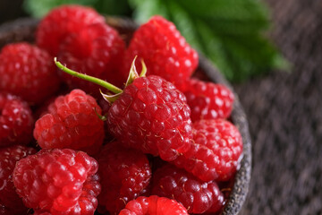 Fresh red raspberries in bowl on wooden dark baskground. Closeup berries background.