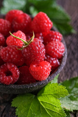 Fresh red raspberries in bowl on wooden dark baskground. Closeup berries background.