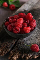 Fresh red raspberries in bowl on wooden dark baskground. Closeup berries background.