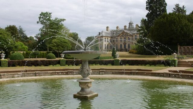 A water fountain in a large pool in the luxurious gardens of a wealthy manor house stately home estate in England
