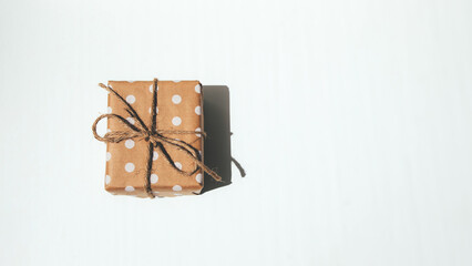 The gift is wrapped in kraft paper with white circles, tied with rope on white background. Top view