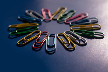 Multicolored paper clips on a blue background. office work. School supplies