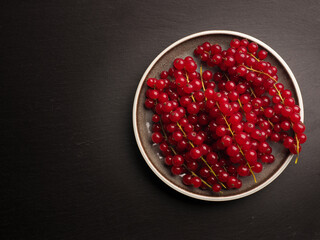 Red currant on a ceramic plate on a dark slate background, view from above with space for text, healthy food concept