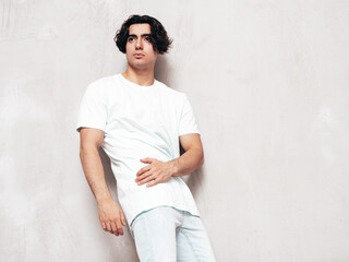 Portrait of handsome confident  stylish hipster lambersexual model.Sexy man dressed in over size T-shirt and jeans. Fashion male isolated in studio. Posing near grey wall