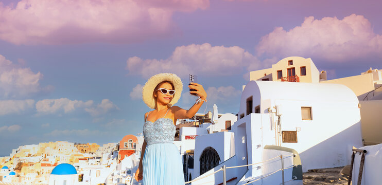 Happy  smiling of  young asian woman in blue dress with  taking selfie at View of  evening scene blue church dome in Oia village,Santorini,Greece