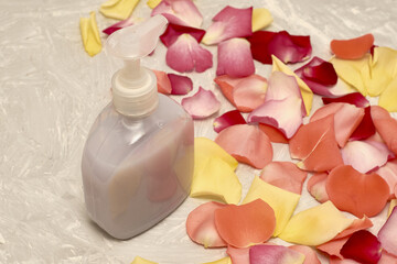 rose petals and a bottle of liquid soap on a gray textured background