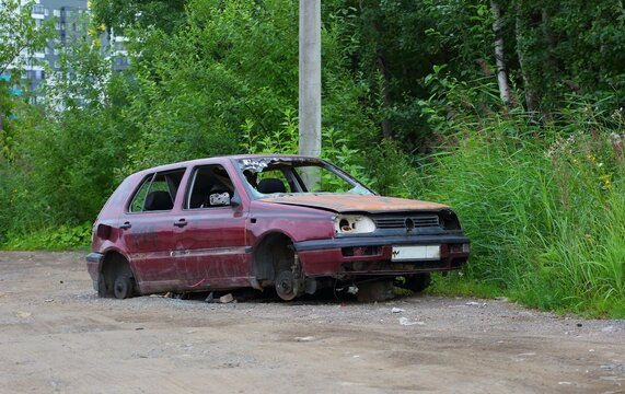 The skeleton of a red broken abandoned car on the side of the road, Warehouse Street, St. Petersburg, Russia, July 2022