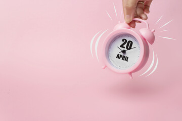 April 20th. Day 20 of month, Calendar date. The morning alarm clock jumping up from the bell with calendar date on a pink background.  Spring month, day of the year concept.
