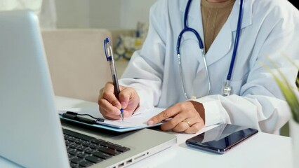 Closeup of doctor or nurse woman in uniform with stethoscope writing information of patient prescription in paperwork on clipboard and typing laptop computer for history record medical document report