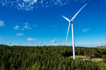 Aerial view on a wind electricity generator in a forest area of Connemara, county Galway, Ireland. Production of clean renewable energy. Industrial object in nature environment. Blue cloudy sky