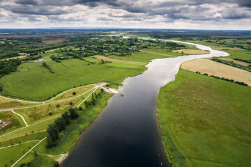 River Shannon flows between green grass fields and agriculture land. Irish landscape. Low cloudy...