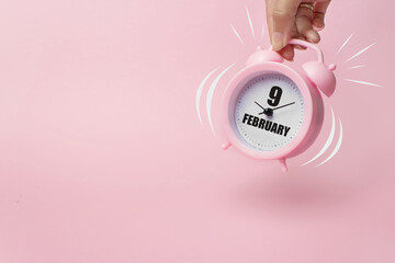 February 9th. Day 9 of month, Calendar date. The morning alarm clock jumping up from the bell with calendar date on a pink background. Winter month, day of the year concept.