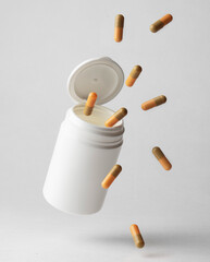 An orange-beige colored pill capsule falling out of a white plastic pill bottle on a light...