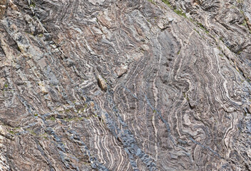 Detail of grey, deformed and curved layers in rock, caused by geological forces, natural background