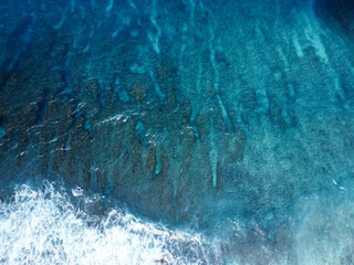 Aerial down shot of crystal clear water and white waves crashing agaist rocks in nusa penida
