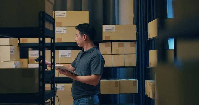 Asian businessman use barcode scanner scan paper box in shelf and put data in digital tablet cut stock online data information detail for express delivery at warehouse. Startup small business concept.