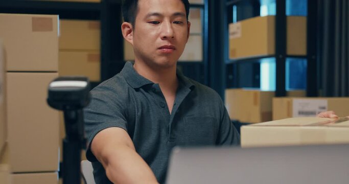 Close-up Asian businessman use barcode machine scan customer data in paper box and type register online information order detail in laptop for express delivery at warehouse. Startup business concept.