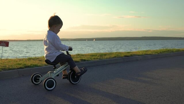 A child rides a tricycle at sunset near the sea