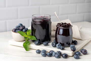 Homemade blueberry raspberry  blackberry jam in glass jar at white table.
