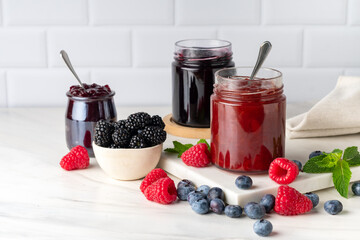 Homemade blueberry raspberry  blackberry jam in glass jar at white table.