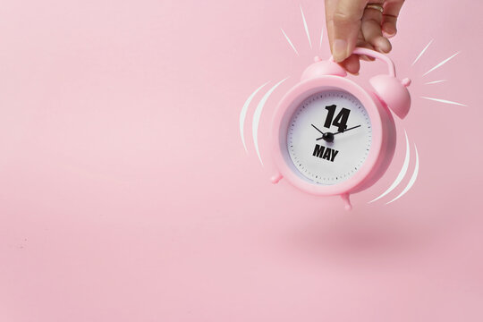 May 14th. Day 14 of month, Calendar date. The morning alarm clock jumping up from the bell with calendar date on a pink background. Spring month, day of the year concept.