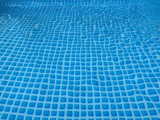 the blue checkered bottom of a pool through the water surface