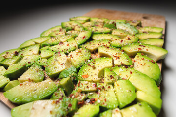 cut avocado into small pieces sprinkled with red spices on a cutting wooden board. food background
