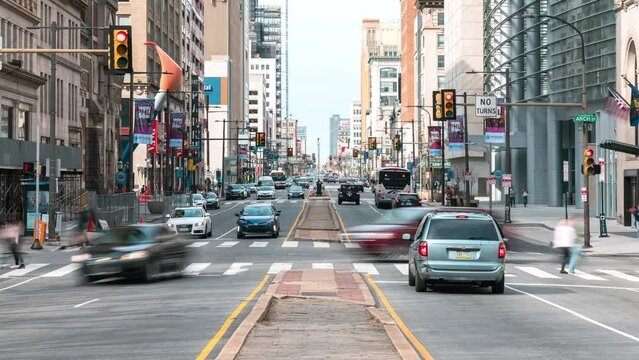 Downtown cityscape time-lapse of car traffic transportation, people walk cross road at junction intersection in Philadelphia, USA. Public transport, American city life, or commuter lifestyle concept