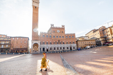 Naklejka premium Morning view on the main square of Siena city with town hall and woman walks with a dog. Concept of architecture of the Tuscan region and travel Italy