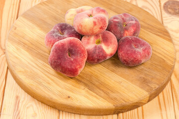 Flat peaches on a round wooden cutting board