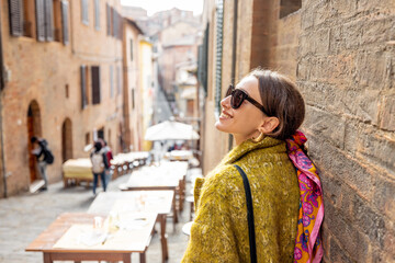 Obraz premium Sylish woman walks on narrow and cozy street in old town of Siena city. Concept of traveling in Tuscany region and italian lifestyle