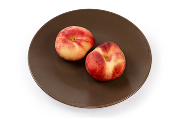 Two flat peaches on the brown dish on white background
