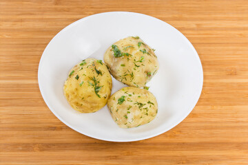 Boiled young potatoes with dill on dish on wooden surface