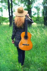 Young woman with guitar walking in the forest on a sunny summer day